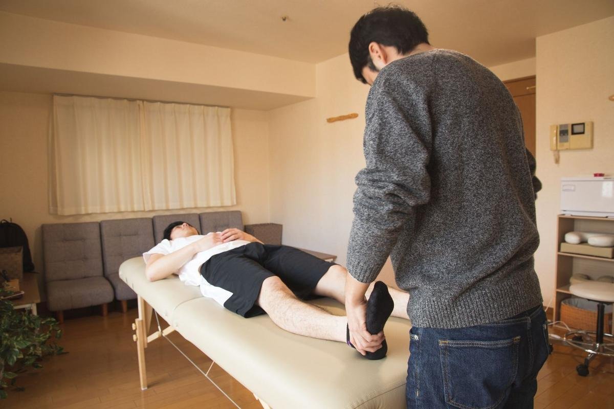 Homme allongé sur table de massage, autre homme manipulant son pied dans une pièce
