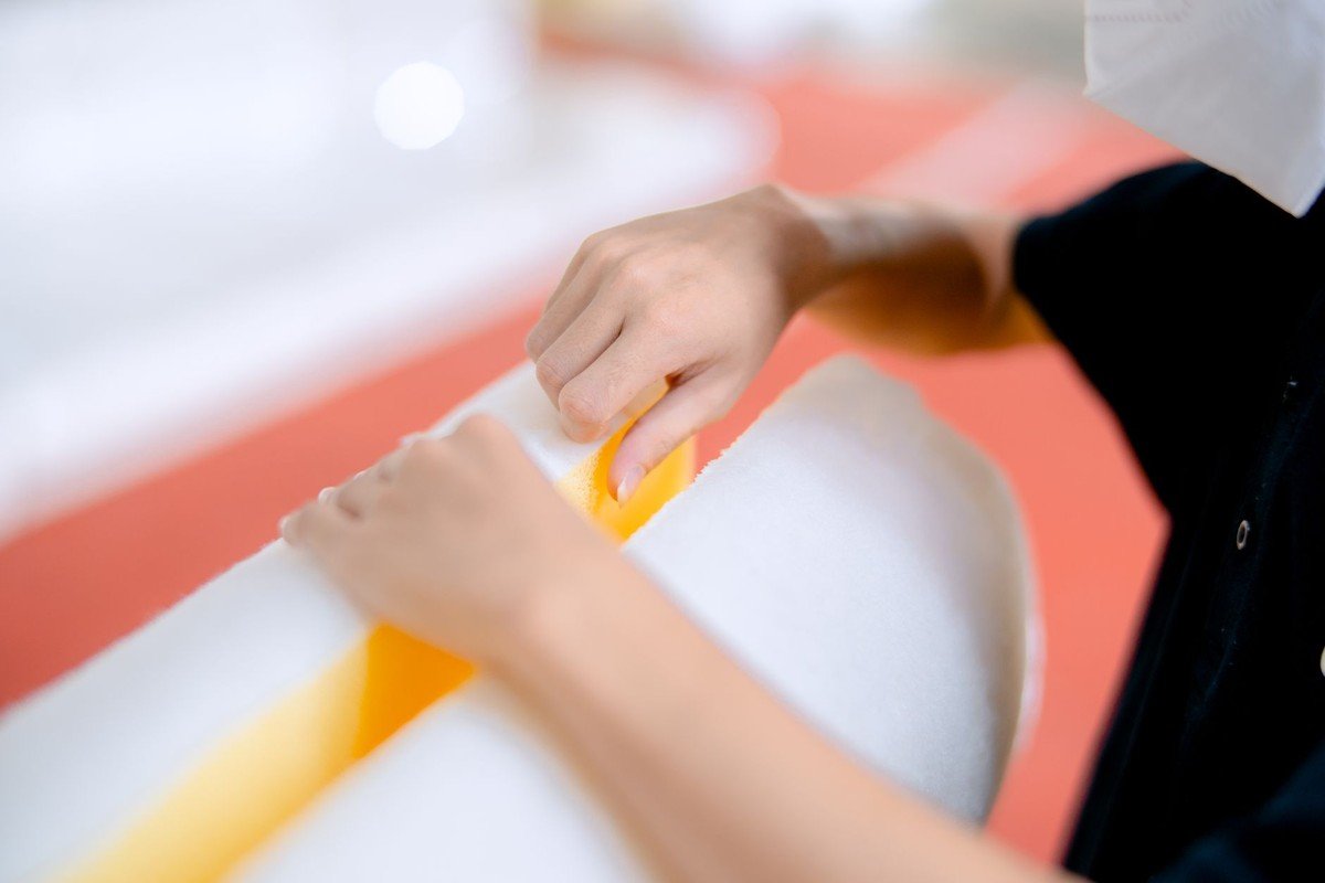 Des mains appliquent un cutter jaune sur un rouleau blanc